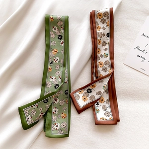Detail of green and brown floral print twilly scarves on soft white fabric background