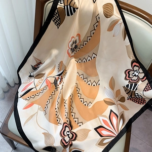 Elegant floral silk-like square scarf in warm almond tones draped on a wooden chair