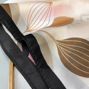 Macro detail of silk scarf showing black stitched edges and earth tone abstract pattern