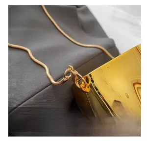 Detail of high-gloss gold lobster clasp and snake chain on a metallic crossbody bag