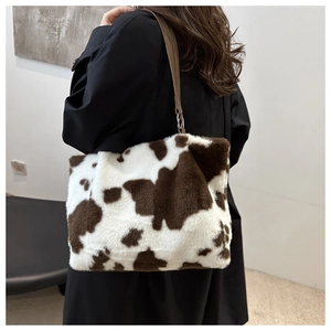 Close-up of fluffy cow print tote bag with brown leather strap and metallic hardware