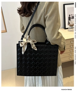 Detail of a large black quilted tote bag with a vintage chain print silk scarf on the handle