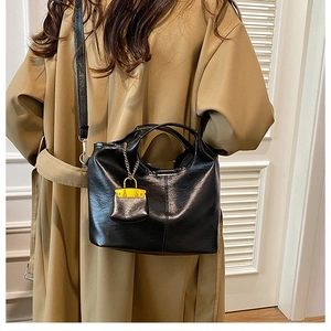 Detail of black leather bucket bag with yellow trim charm and long strap on trench coat