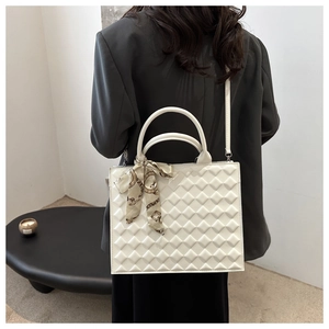 Detail shot of white quilted crossbody bag with silk scarf on handle and sleek gold rings