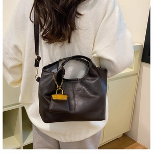 Detail of soft dark brown leather tote bag with mini charm on white sweater background
