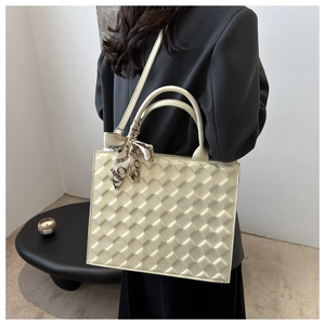 Close-up of a cream quilted tote bag with a decorative chain-print silk scarf on the handle