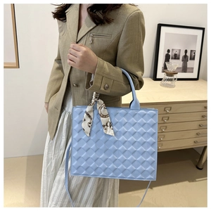 Detail of light blue quilted square handbag with silk scarf on a stylish olive blazer