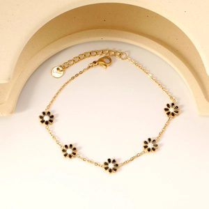 Gold stainless steel daisy charm bracelet with black and white petals on minimalist background