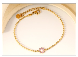 Close-up of stainless steel gold bead bracelet with purple enamel flower and lobster clasp