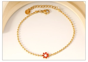 Macro detail of golden stainless steel beaded bracelet featuring a red floral pendant charm