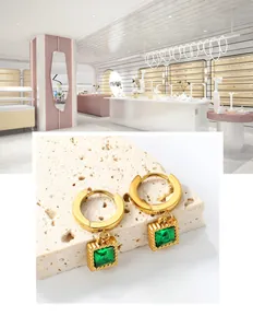 Détail de boucles d'oreilles carrées en zircon émeraude doré sur pierre beige texturée
