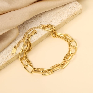 Minimalist double-layered 18K gold heart bracelet with cuban chain on beige stone background