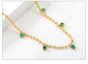 Macro detail of 18K gold stainless steel bead chain with emerald green round gemstones