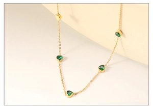 Macro detail of gold necklace featuring five evenly spaced heart-cut emerald green stones