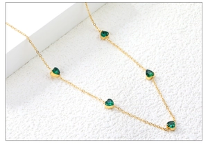 Detailed close-up of gold chain necklace featuring five green heart-shaped zircons