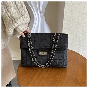 Macro detail of black quilted texture and silver chain strap on a rectangular shoulder bag