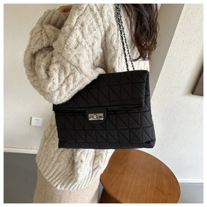 Close-up of black quilted chain bag with silver twist lock and leather strap detail