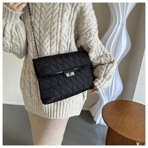 Close-up of black quilted chain bag with silver clasp worn on a white knit sweater