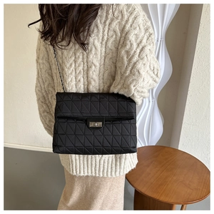 Detail view of quilted black shoulder bag with silver chain strap and metal clasp closure
