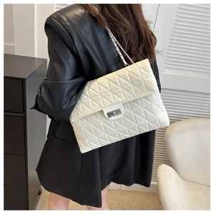 Detail of a large beige quilted chain bag with silver lock worn with a black leather blazer