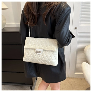 Detailed view of beige quilted leather crossbody bag with silver rotating lock on model