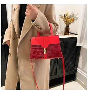 Detail of red crocodile texture handbag with gold twist lock worn with beige coat