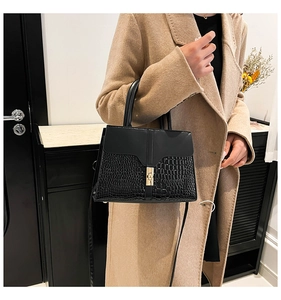 Detail of black faux crocodile leather handbag with gold metal clasp on beige coat