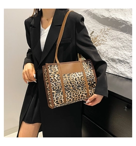 Detail view of large leopard print tote bag with brown straps worn over a black blazer