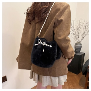 Détail du sac seau en fausse fourrure noire avec nœud blanc décoratif et chaîne perlée