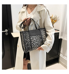 Détail d'un sac cabas léopard avec lanières en cuir noir porté sur un trench-coat blanc