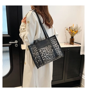 Detail of leopard print tote bag with black leather handles shown on a model
