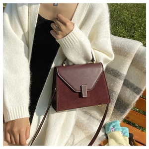 Detail of burgundy patchwork Kelly bag with suede texture and metal clasp on park bench