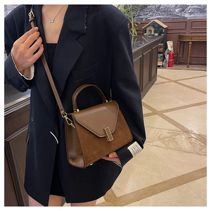Detail of dark brown matte patchwork handbag with golden clasp worn by a model