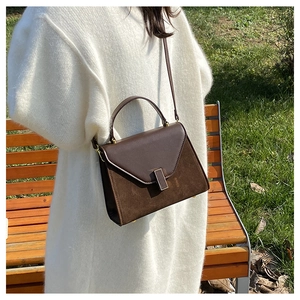 Brown leather Kelly style bag with metal buckle worn by model in autumn outdoor setting