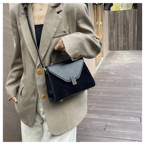 Outdoor model display of matte and smooth black leather trapezoid bag with gold buckle