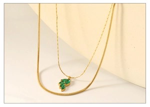 Detail of layered gold necklace with emerald green zircon leaf pendant and flat snake chain
