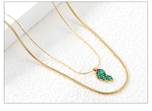 Macro shot of double-layer gold necklace with green zircon leaf pendant on stone background