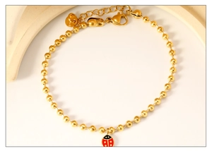 Détail d'un bracelet doré à perles avec charm coccinelle en émail rouge et fermoir