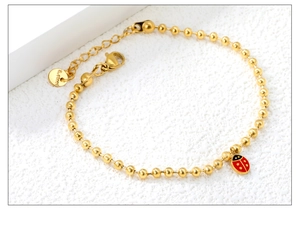 Détail d'un bracelet boule en acier doré avec pendentif coccinelle en émail rouge