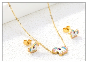 Detailed close-up of unicorn enamel jewelry set including necklace and studs on sand