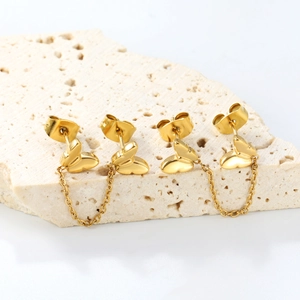 Elegant gold butterfly stud earrings with wheat chains on a beige stone surface