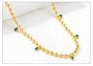 Detail of 18K gold bead chain necklace with green teardrop zircon charms on white surface