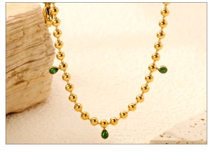Detailed close-up of golden beaded necklace featuring three green teardrop zirconia pendants