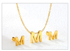 Detail of gold letter M jewelry set including necklace and stud earrings on white pedestal