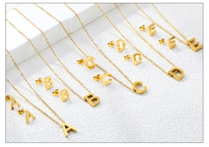 Close-up of golden A-E capital letter jewelry set including necklaces and stud earrings