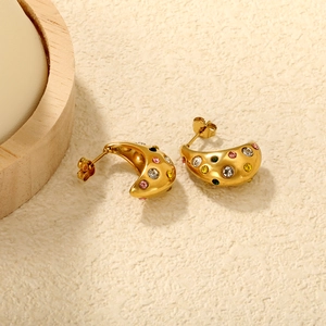 Detail of 18K gold earrings with colorful rhinestones on a textured stone surface