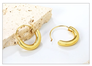 Detailed view of polished chunky golden hoop earrings on a natural stone background