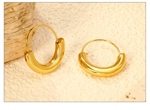 Close-up of chunky gold-plated C-shaped hoop earrings on textured stone surface