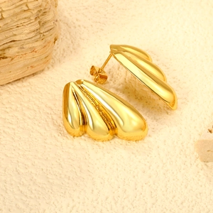 Minimalistische goldene Flügel-Ohrstecker mit polierter Oberfläche auf Naturstein-Hintergrund