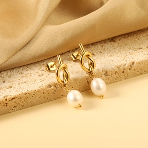 Boucles d'oreilles nœud doré élégantes avec perle sur support en pierre texturée
